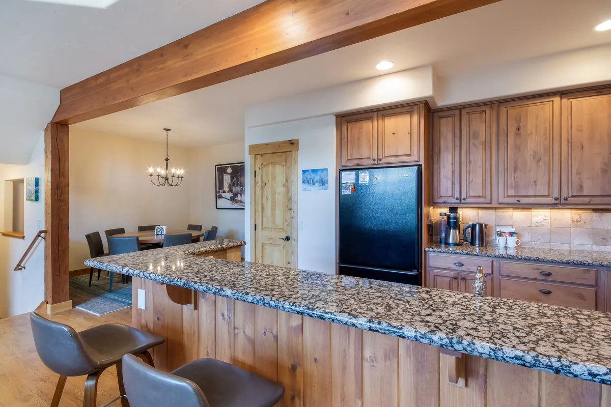A warm, open kitchen with granite countertops, wood cabinetry, a visible dining area, and an elegant chandelier overhead. The space is designed for both cooking and socializing, with plenty of room for multiple people to move and work together.