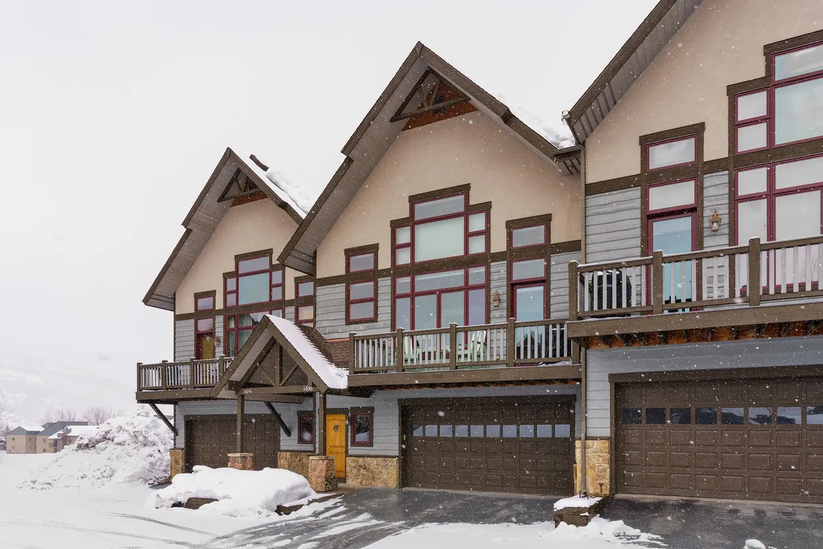 This image highlights the chalet's large windows, balcony, and architectural details with a snowy backdrop. The scene suggests guests enjoying winter sports, watching snowfall from the comfort of the balcony, or hosting après-ski gatherings.