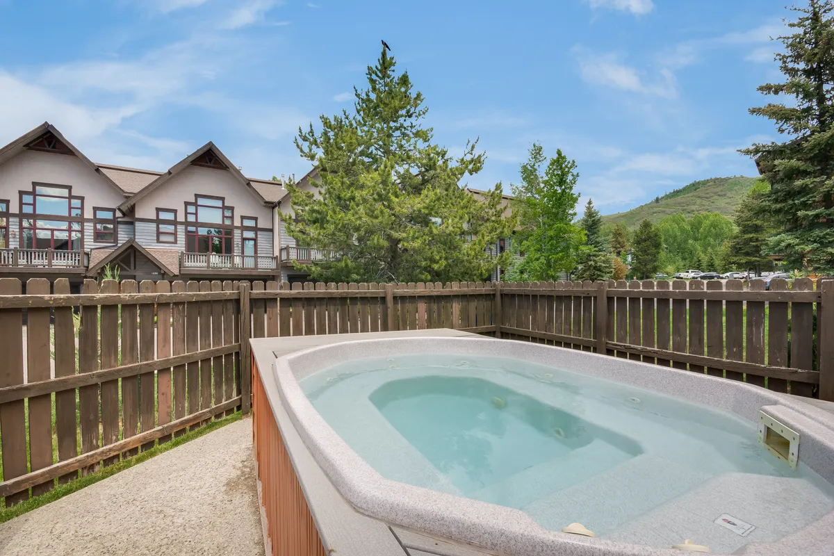 A deck scene featuring a hot tub, fenced yard, trees, and stunning mountain views in the background. The space feels tranquil, offering both a place to relax outdoors and a direct connection to the alpine setting.