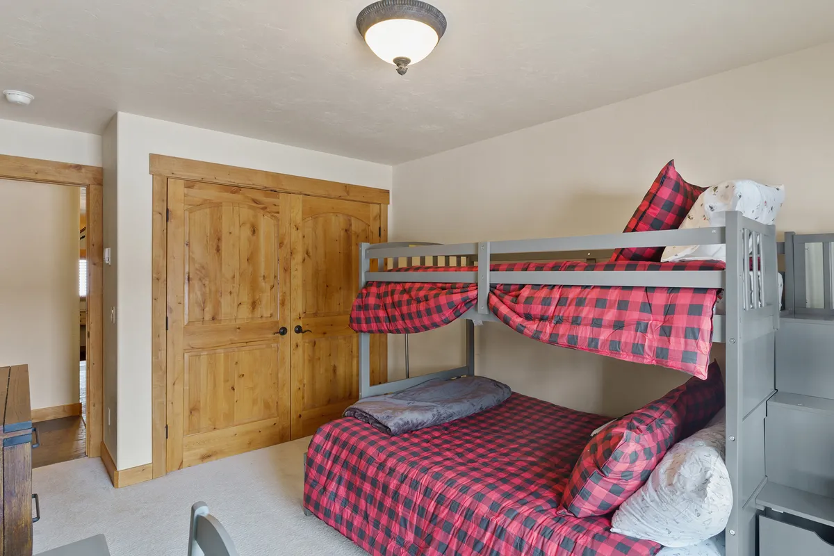 A cheerful bunk room featuring twin-over-full bunk beds with plaid bedding, wooden closet doors, and a cozy, playful atmosphere perfectly suited for kids and younger travelers.