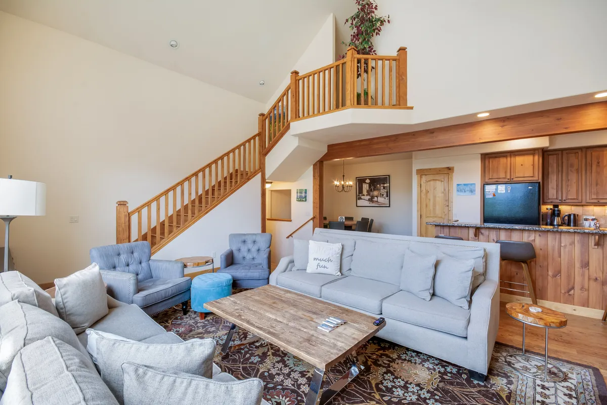 The image showcases a beautifully designed open-concept living space featuring plush sofas surrounding a modern coffee table, a stylish staircase, and a seamless connection to a fully equipped kitchen—perfect for gathering and socializing.