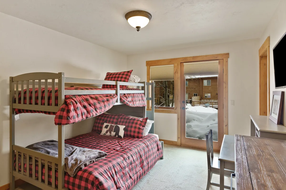 A bunk room with a twin-over-full bunk bed, a window view of the outdoors, and a small desk. The playful and cozy vibe is suitable for children, teens, or grandparents, with details like the reading nook and ample natural light.
