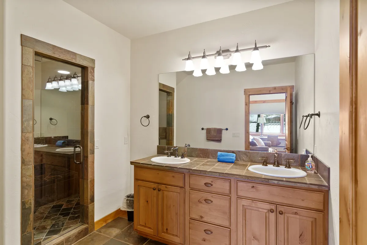 A calming, spacious bathroom with a double sink vanity, large mirror, shower area, and wooden cabinetry, offering a serene retreat for relaxation after a day of adventure.