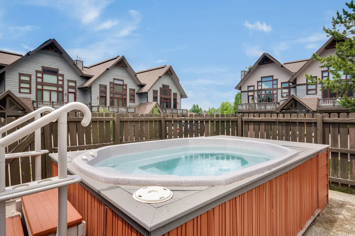 This exterior image showcases the community hot tub surrounded by a fence and neighboring buildings. The inviting atmosphere suggests relaxation and socializing, with the hot tub as the focal point for après-ski or evening unwinding.