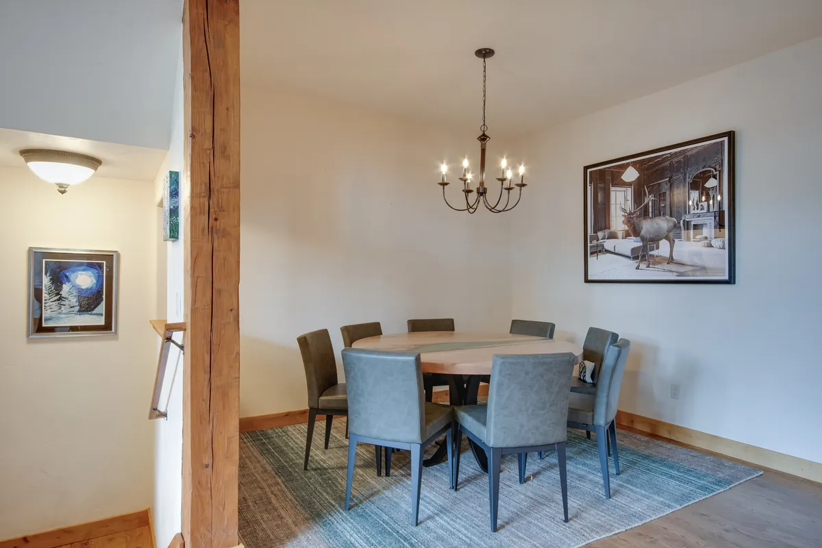 A round dining table set beneath a shimmering chandelier, surrounded by inviting chairs and framed artwork that adds a touch of warmth and style. The mood is festive and perfect for family dinners or celebrations.