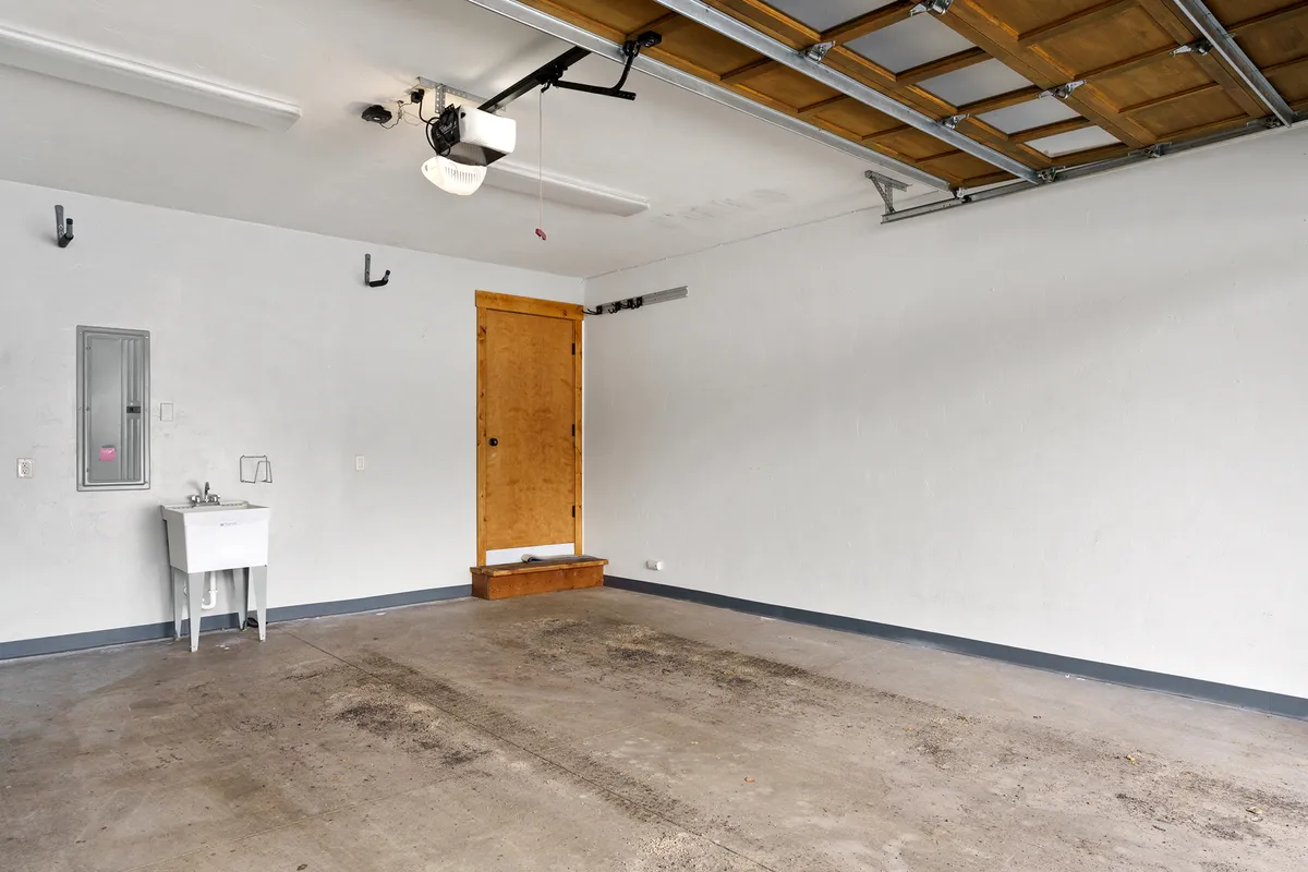 A view of the garage interior, showing the garage door opener, a utility sink, and a wooden door. The organized, functional space hints at secure storage for gear, tools, and easy access after outdoor activities.