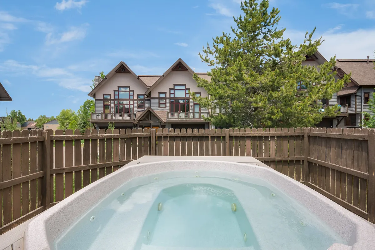 This exterior image features a hot tub set amidst trees and buildings, surrounded by a fence for privacy. The setting exudes calm and invites socializing or unwinding after an active day, with glimpses of sunset light filtering through the trees.