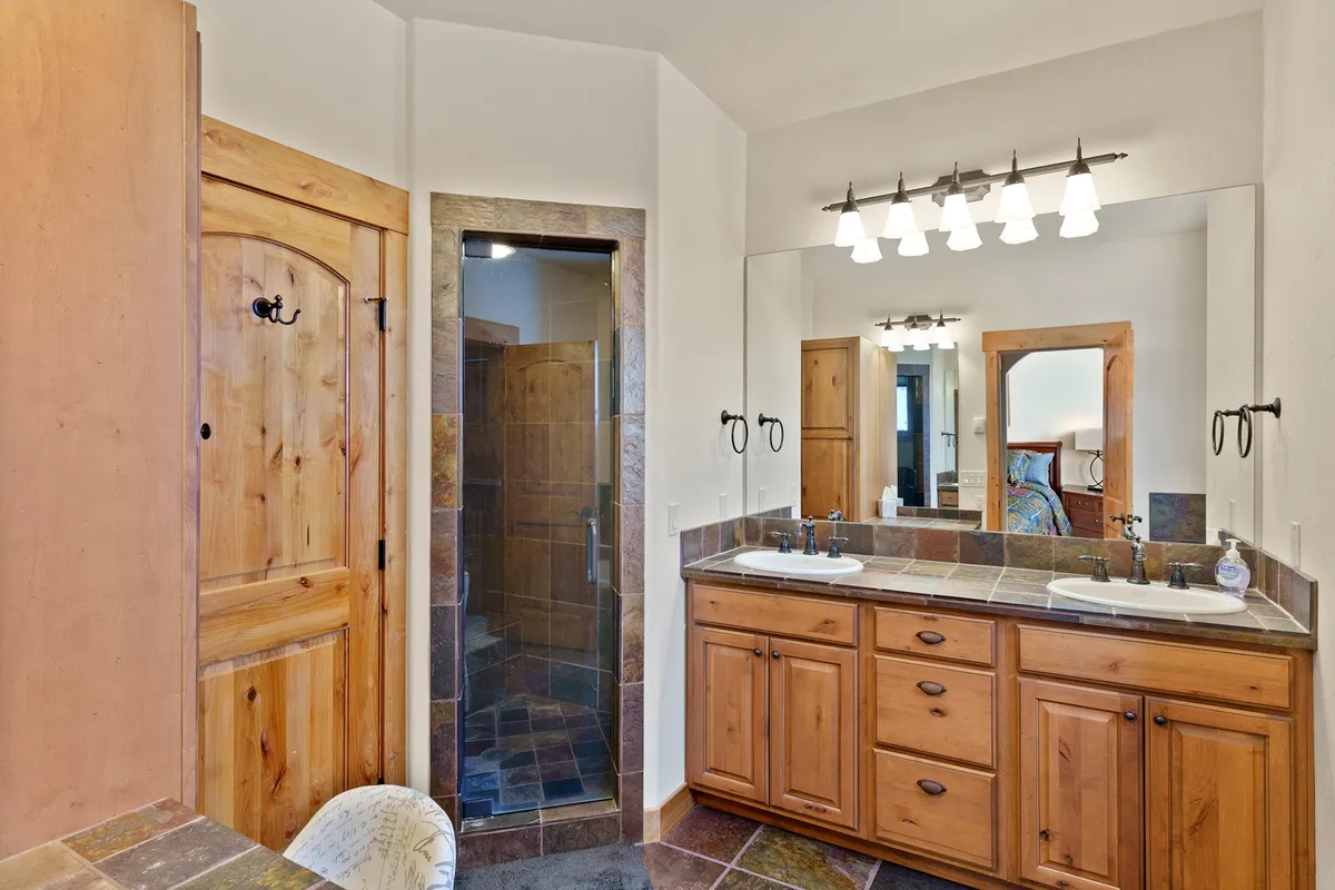 An interior bathroom scene with a double sink vanity, walk-in shower, and natural wood cabinetry. The space feels calm and spa-like, emphasizing modern comforts and a soothing environment for post-adventure relaxation.