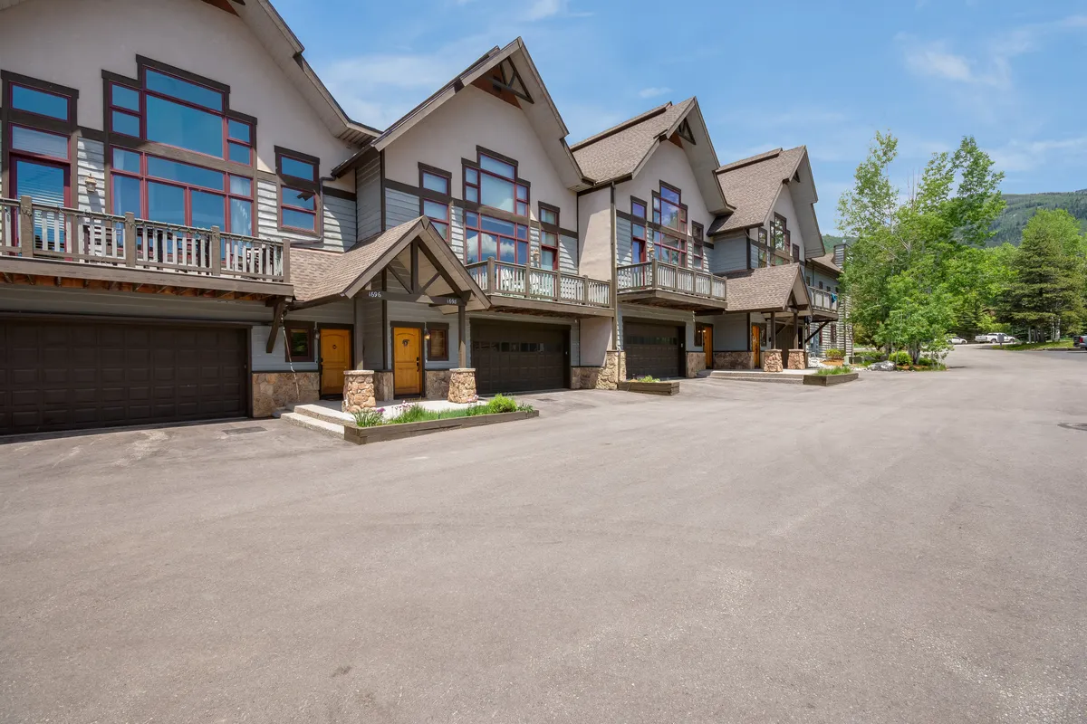 A view of the property's modern exterior with large windows and prominent front doors, set against a mountain backdrop. The communal spaces and inviting design signal a welcoming home base for group activities and nearby adventures.