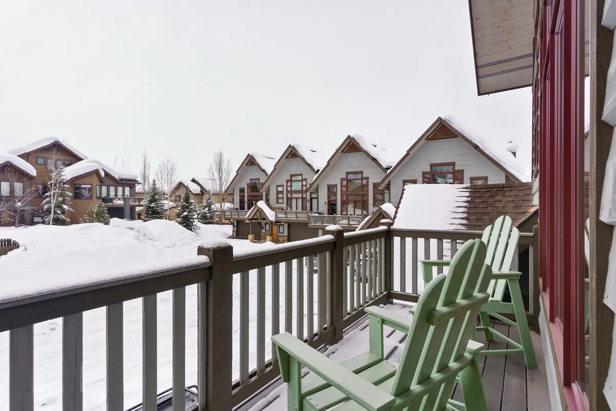 An exterior winter view featuring green Adirondack chairs on a snow-covered balcony, with neighboring homes in sight. The scene evokes cozy moments spent sipping hot drinks and enjoying the snowy Steamboat landscape.