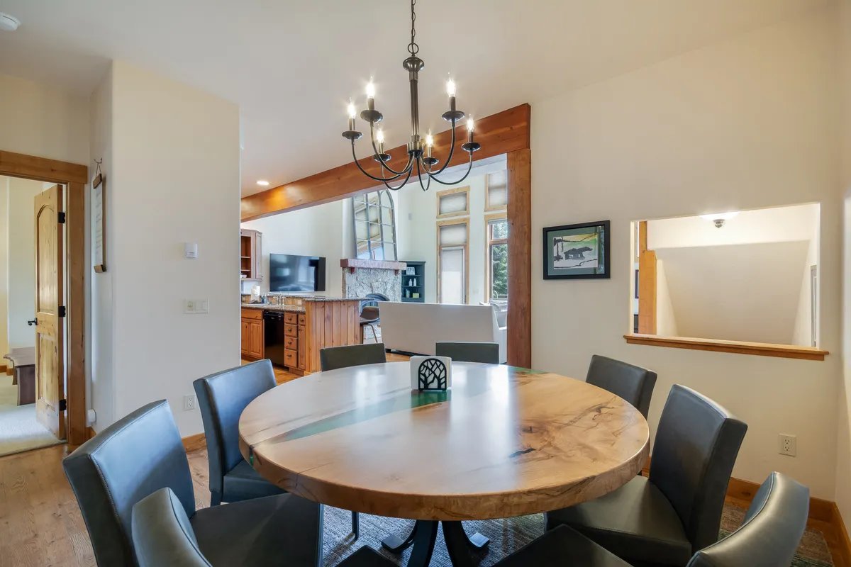 A warm, inviting dining area with a round wooden table set beneath a chandelier, adjacent to an open kitchen. The setup radiates comfort and sets the scene for family meals and gatherings after days spent exploring.